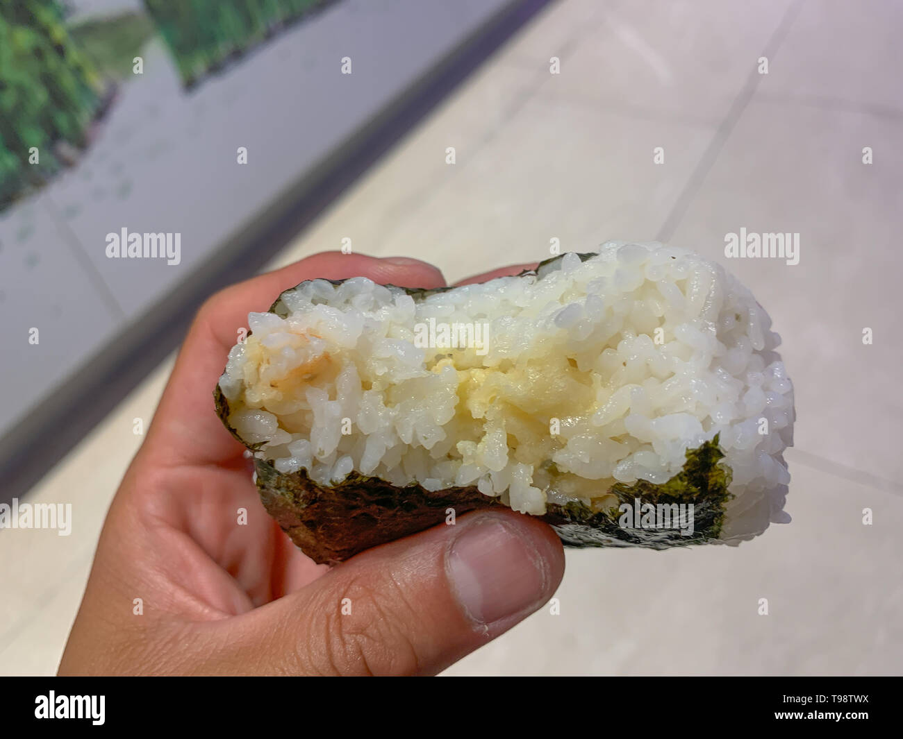 Mano trattiene un parzialmente mangiato tonno e maionese Onigiri. Onigiri è un popolare snack in Giappone. Che di solito può essere trovato nella zona deli di giapponese gr Foto Stock