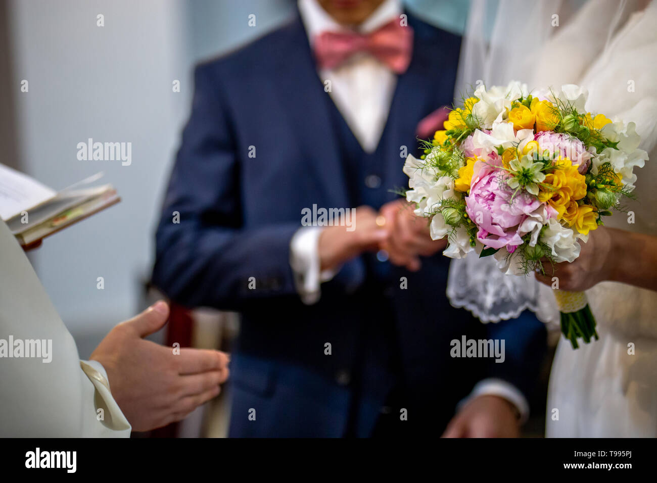 La sposa detiene un matrimonio bouquet di fiori nella sua mano. Il bouquet è composto di bianco, giallo e fiori di colore rosa. Sacerdote canto e lo sposo è I Foto Stock