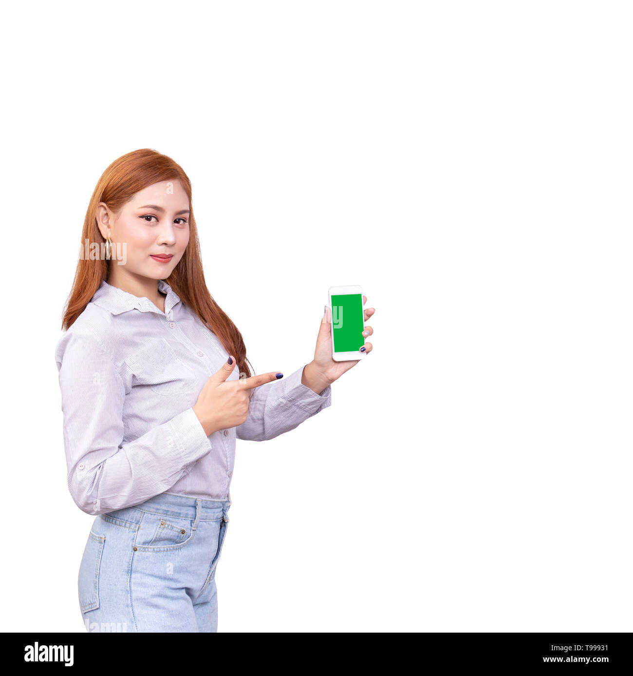 Sorridente donna asiatica in piedi nella camicia casual tenendo il telefono cellulare e il dispositivo di puntamento su smartphone isolato su sfondo bianco con tracciato di ritaglio Foto Stock