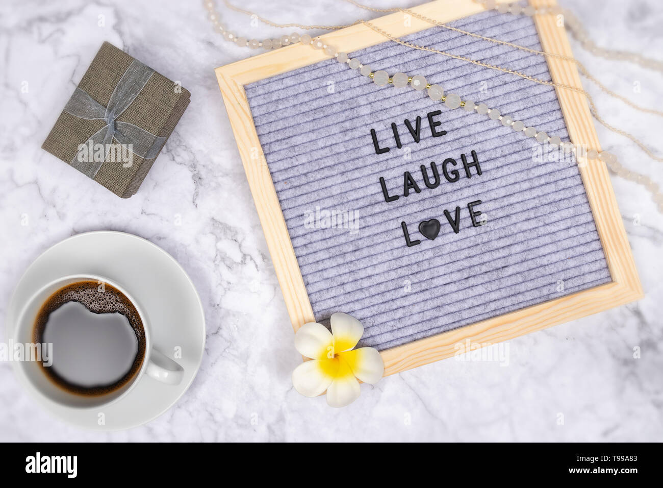 Parola vivere ridere amore sulla lettera di bordo su marmo bianco sfondo scrivania con tazza di caffè e confezione regalo , della decorazione con fiore e luxury pink collana Foto Stock