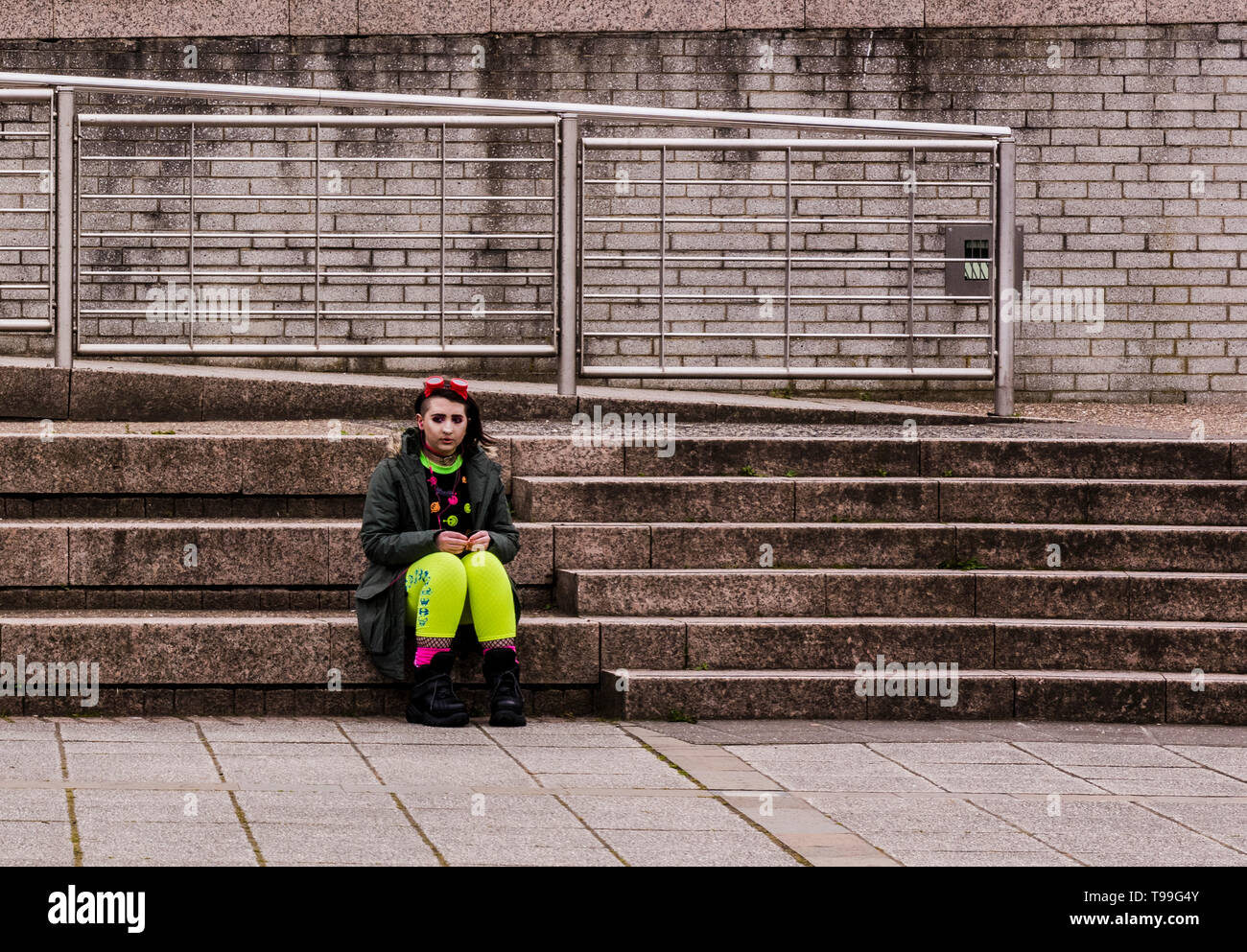 Giovane donna che indossa abiti colorati, seduti sui gradini, espressione triste, Quayside, Newcastle upon Tyne, England, Regno Unito Foto Stock