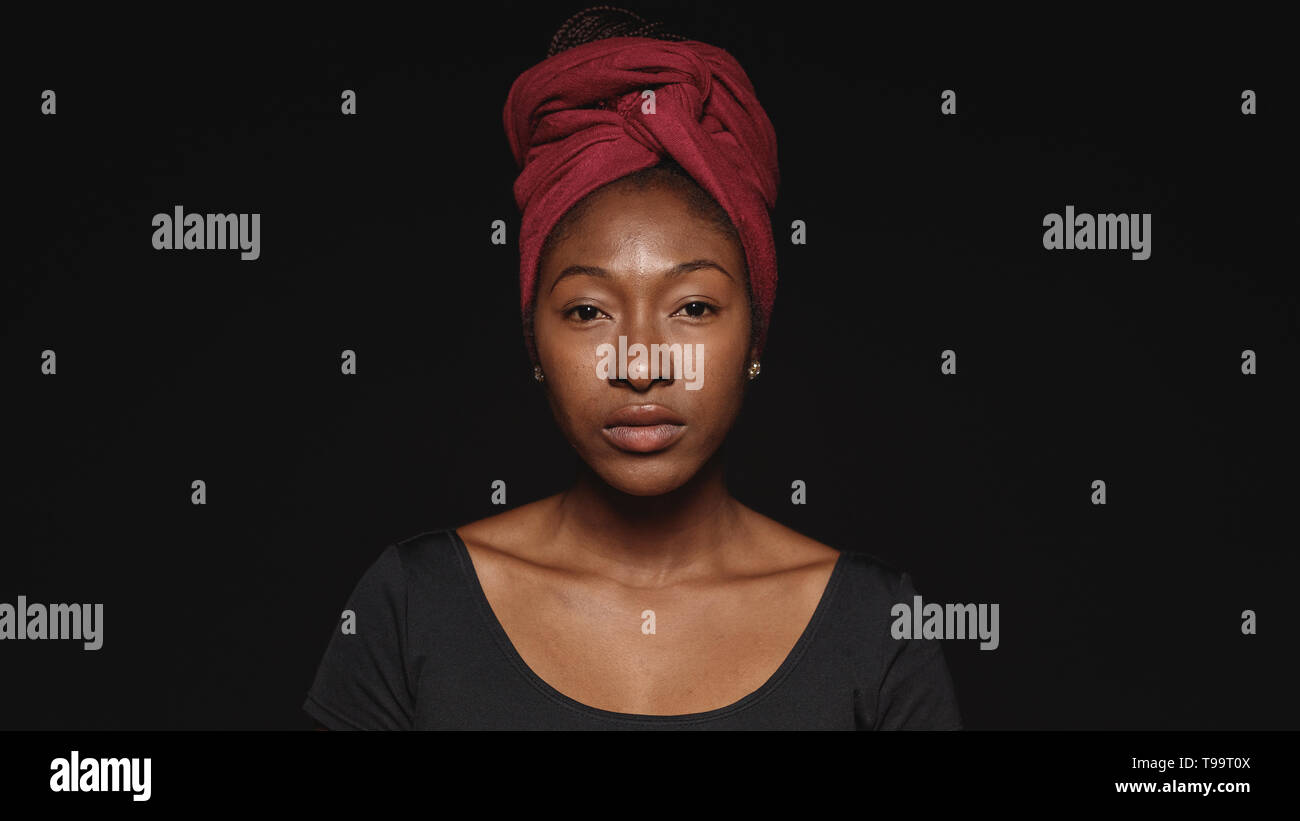 Close up della donna africana isolato su sfondo nero. Femmina africana con una sciarpa avvolta sulla testa guardando la fotocamera. Foto Stock