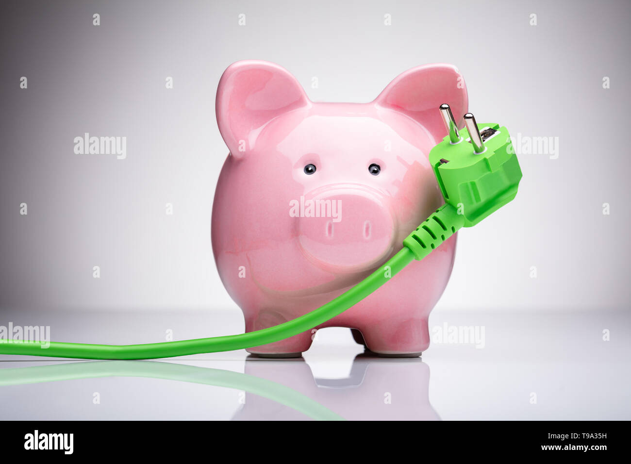 Green Power Plug e Rosa Salvadanaio sulla scrivania riflettente Foto Stock