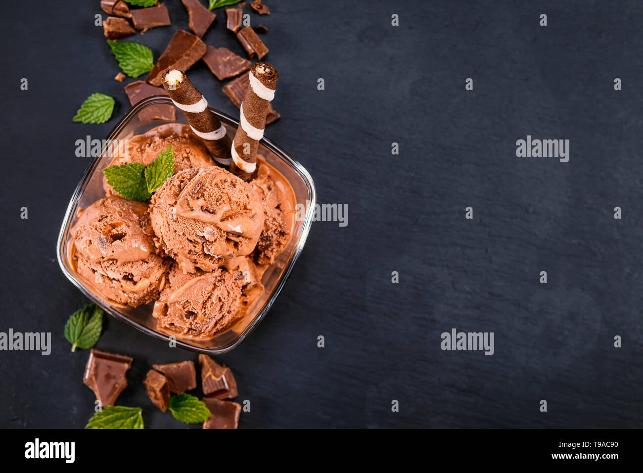 Palline di gelato al cioccolato in recipiente di vetro con bastoncini di wafer, il cono e il cioccolato su un nero ardesia bordo. Focus sulla ciotola con palline di gelato al cioccolato Foto Stock