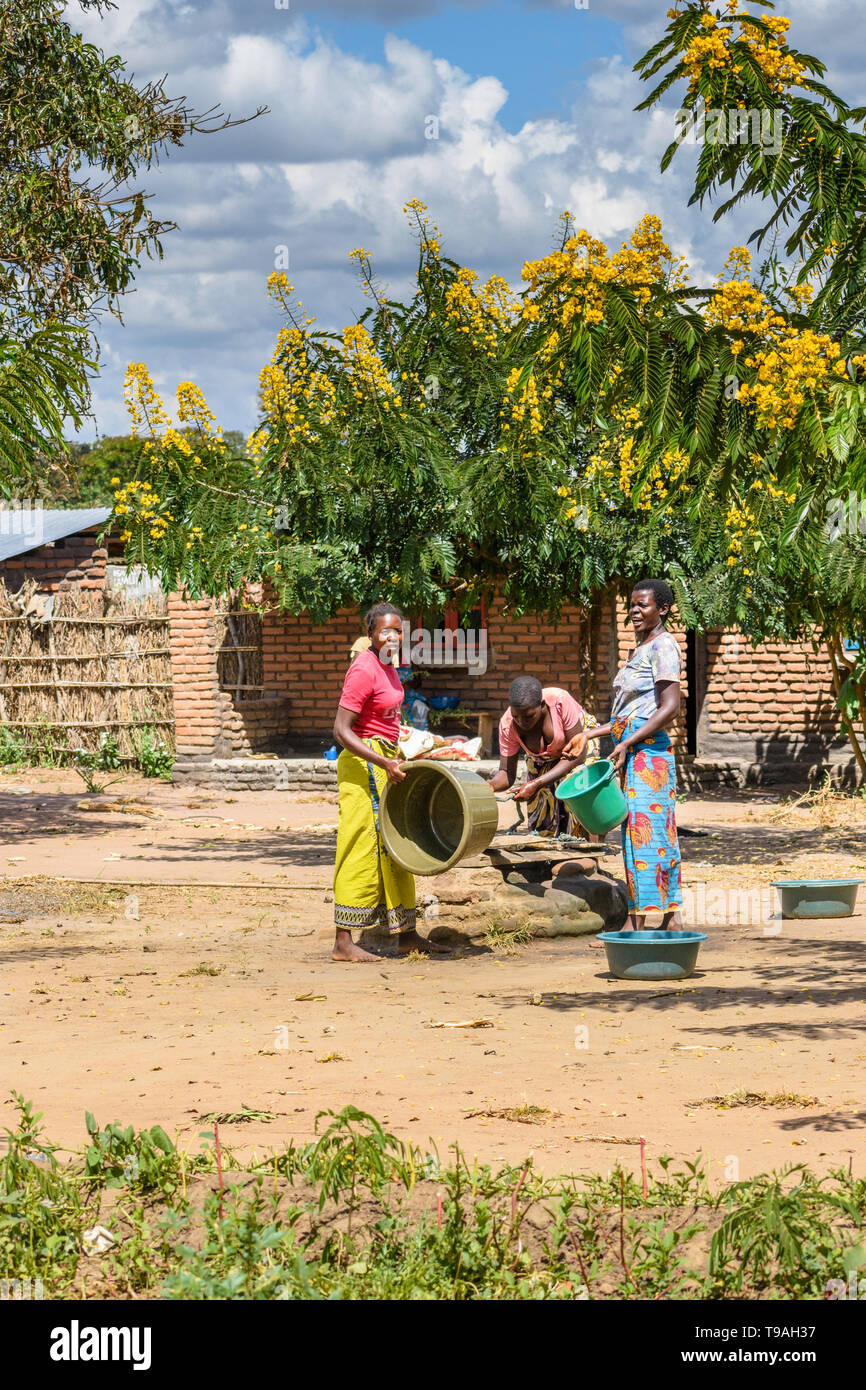 Le donne del Malawi il prelievo di acqua nel sole di mezzogiorno da un pozzetto poco profondo in un villaggio utilizzando secchielli in plastica e la corda Foto Stock