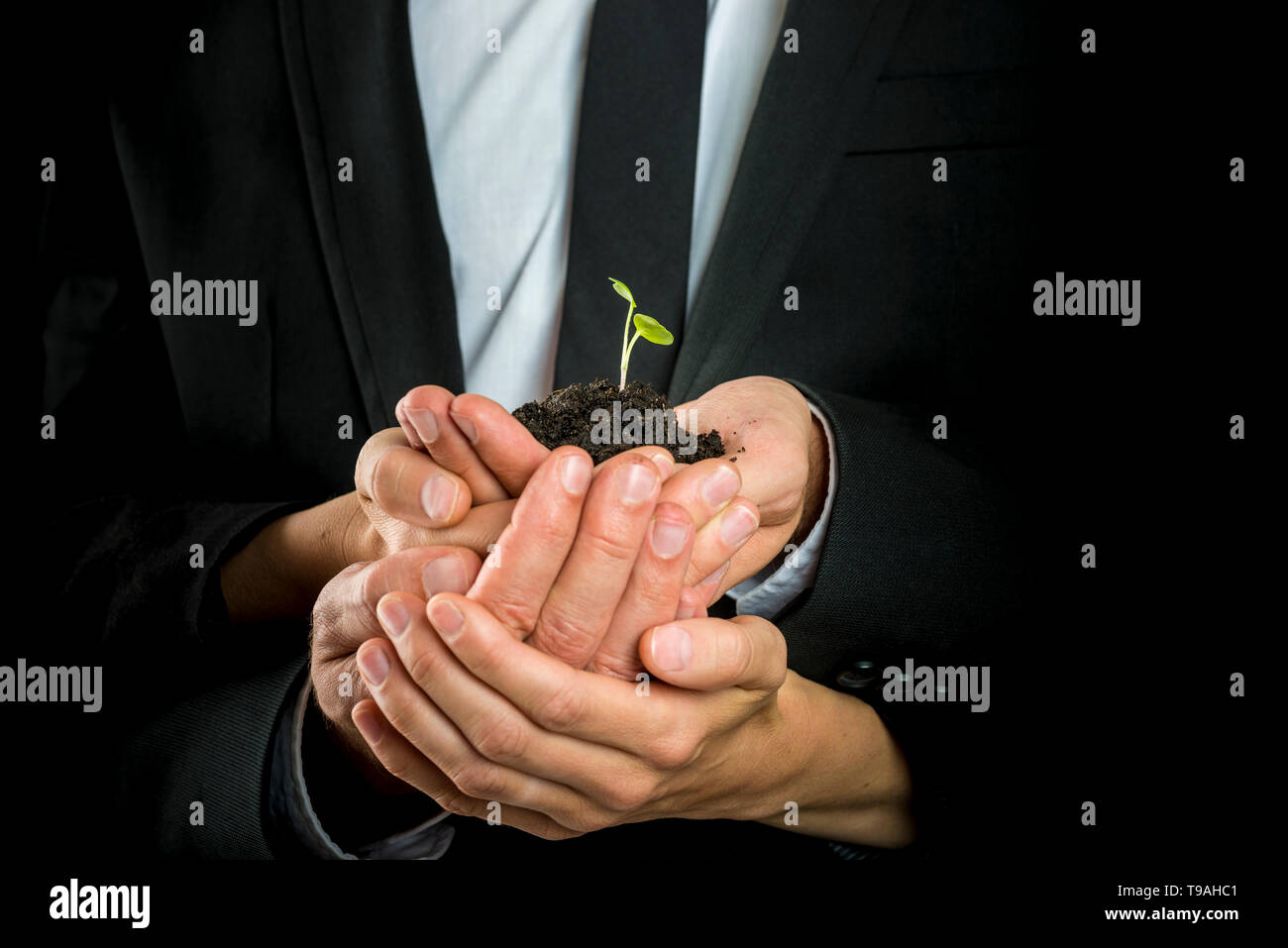 La visione aziendale, avvio o il concetto di lavoro di squadra - maschio e femmina business partner per imbutitura di un germoglio verde in un pizzico di suolo fertile. Foto Stock