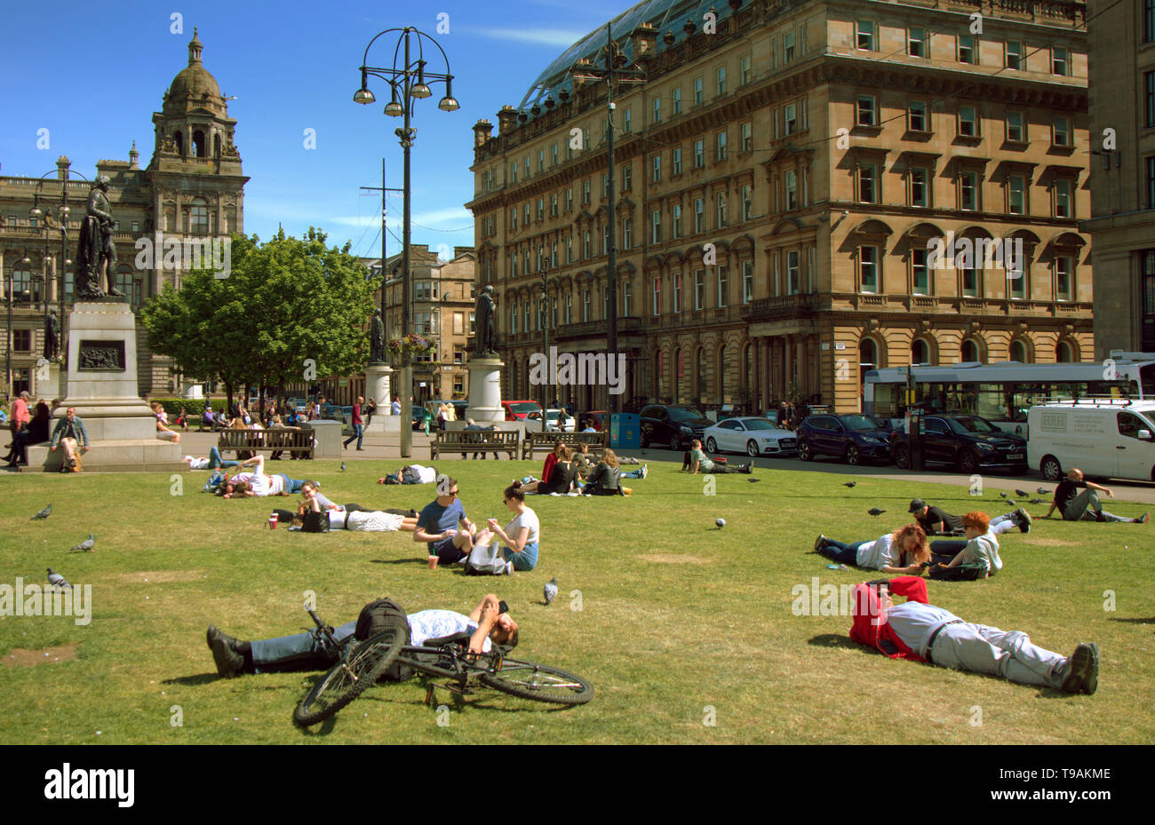 Glasgow, Scotland, Regno Unito, 17 maggio 2019, UK Meteo. Sunny scorcher di un giorno per la gente del posto e i turisti condividono l'erba con i piccioni nel centro civico della città George Square. Credito traghetto Gerard/Alamy Live News Foto Stock