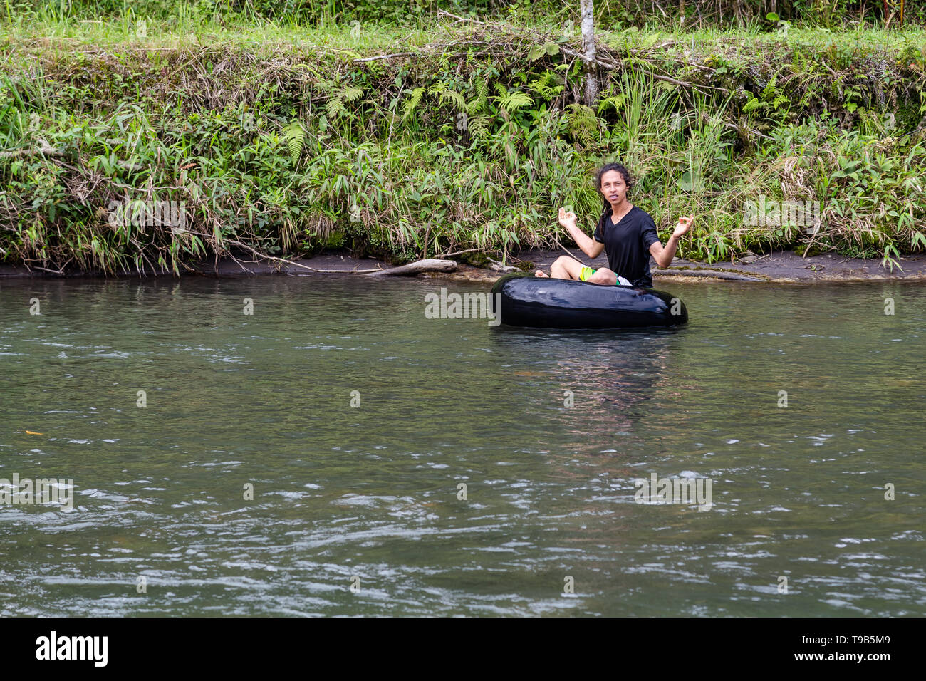 Giovane maschio ispanica medita sulla boa galleggiante sul fiume Foto Stock