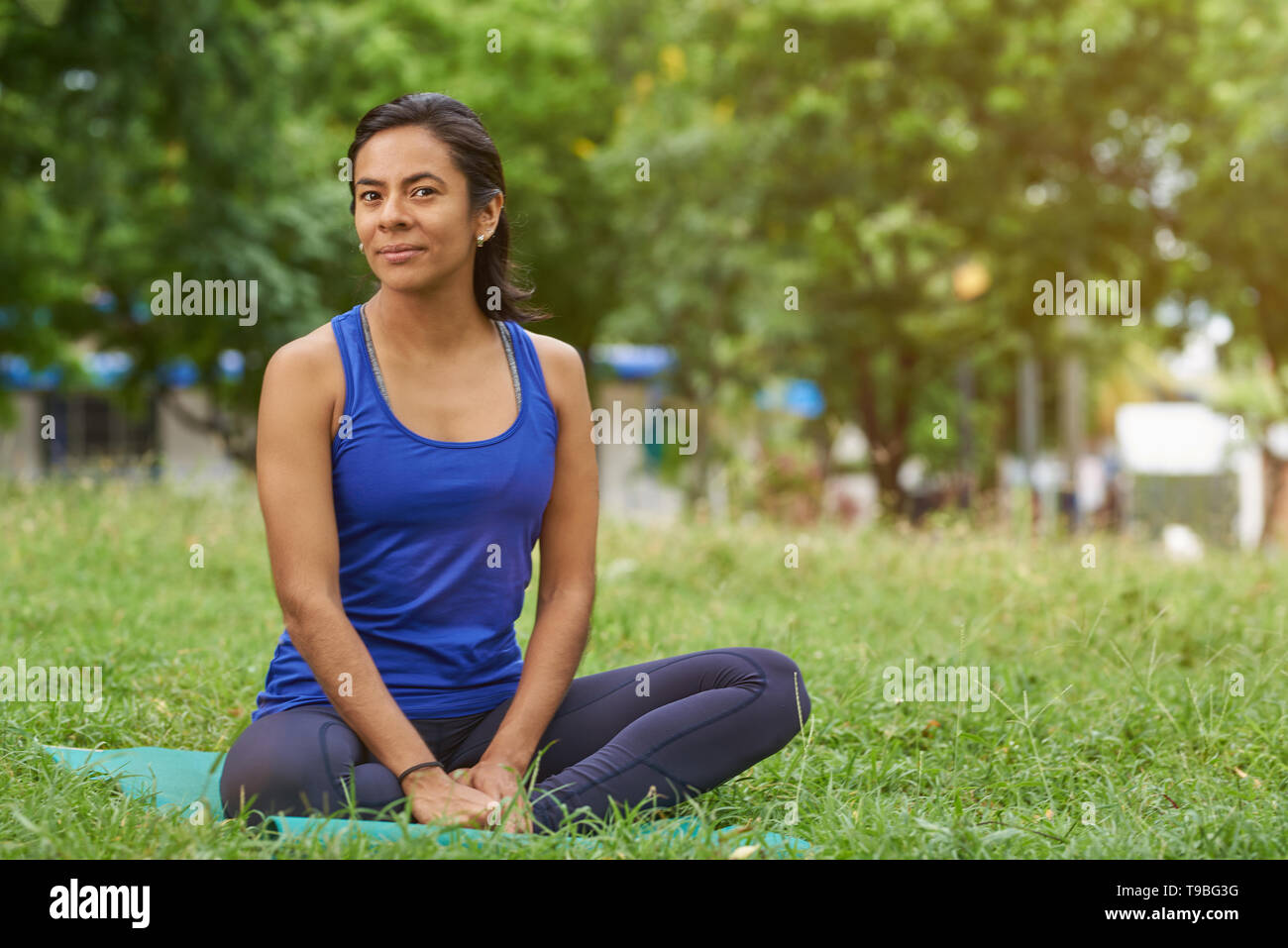 Pretty skinny sportivo da donna giovane seduto sul materassino yoga in estate verde sullo sfondo del parco Foto Stock