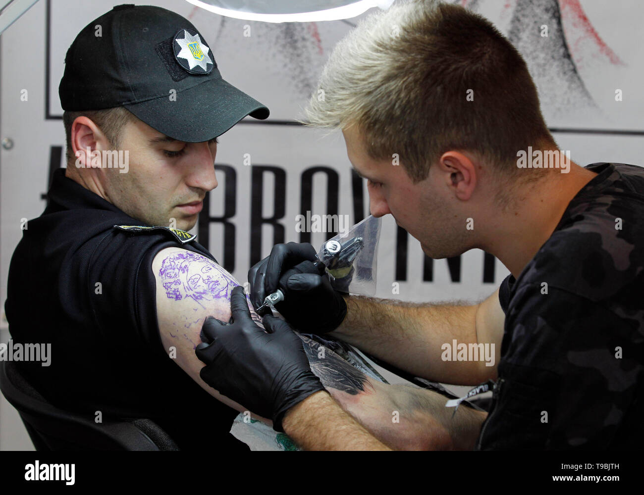 Un tatuaggio artista è visto lavorare su un funzionario di polizia durante il tatuaggio di raccolta presso l annuale xv International Tattoo Convention di Kiev. Il tatuaggio festival raccoglie i professionisti, gli appassionati e gli intenditori di arte del tatuaggio dal 17 al 19 maggio 2019 a Kiev. Foto Stock