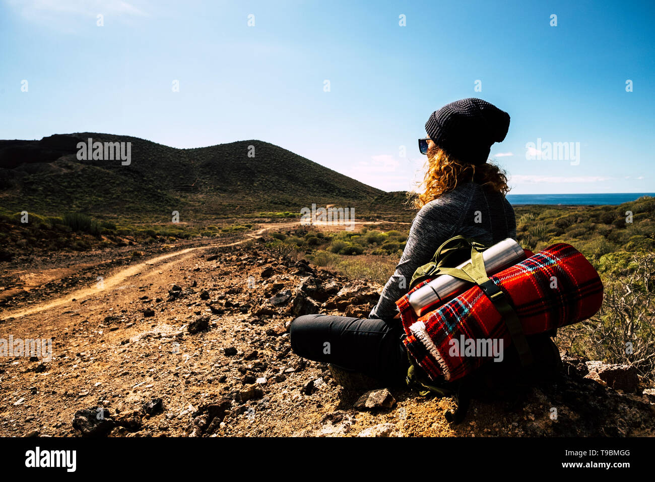 Persone e zaino da trekking avventuroso viaggio attività - donna bionda sedersi e riposare guardando lo splendido paesaggio panoramico con vista del mare e della valle Foto Stock