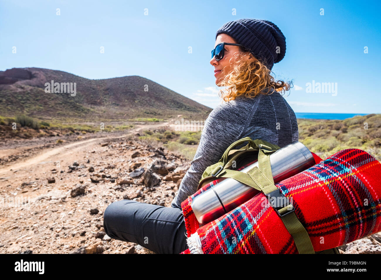 Persone e zaino da trekking avventuroso viaggio attività - donna bionda sedersi e riposare guardando lo splendido paesaggio panoramico con vista del mare e della valle Foto Stock