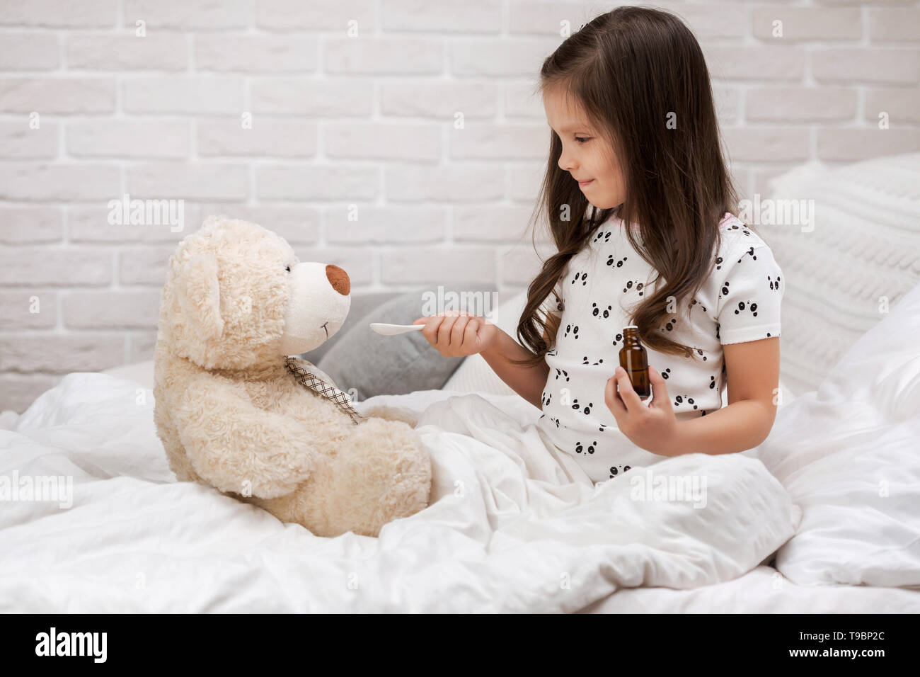 Carina ragazza bambino la riproduzione medico con Teddy bear a casa. ragazza ascolta uno stetoscopio per giocattolo. Foto Stock