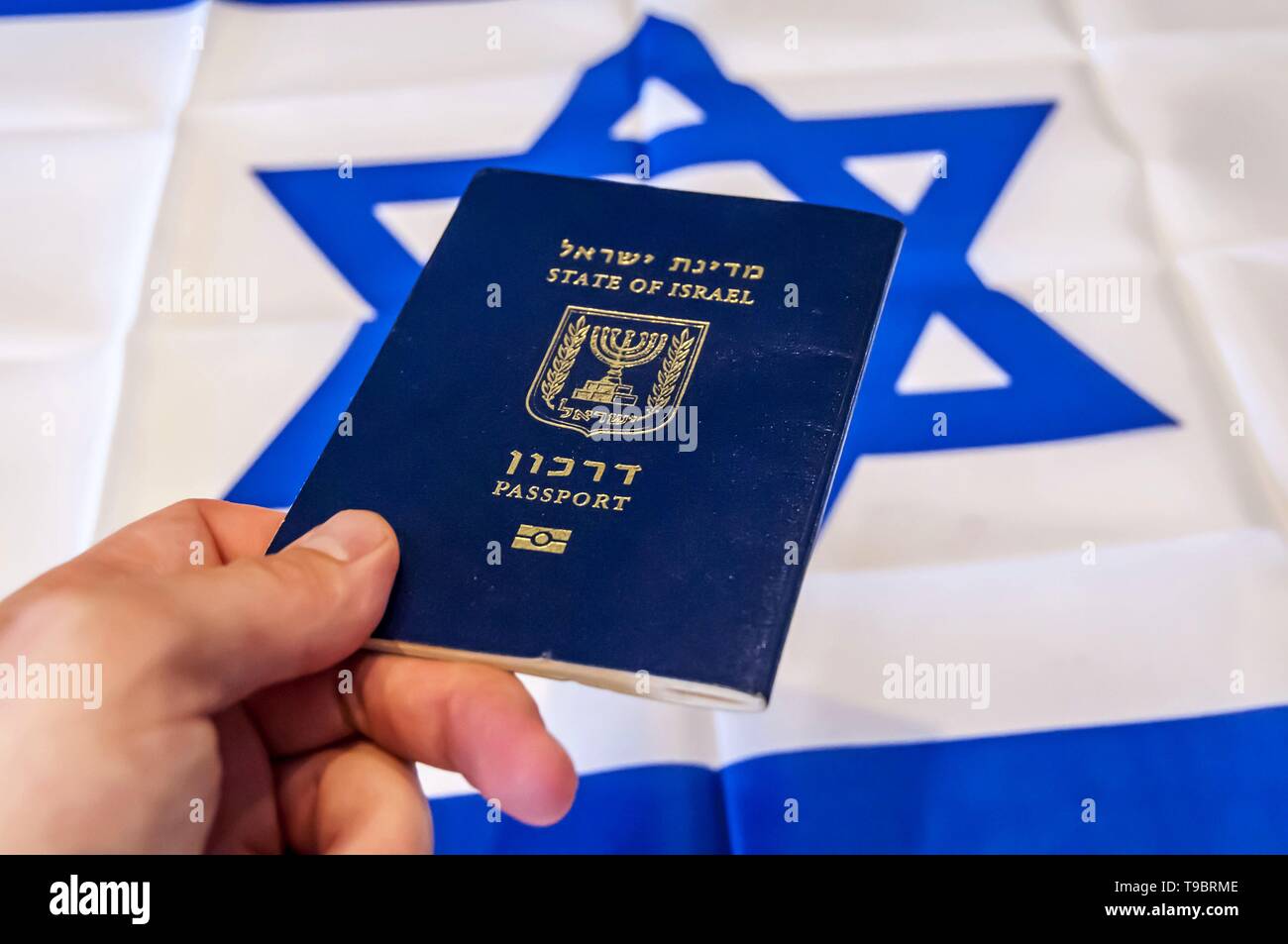 Mano che tiene il passaporto dello Stato di Israele, bandiera Israeliana sullo sfondo. Israele il concetto di cittadinanza, israeliano "biometrici arkon passaporto" Foto Stock