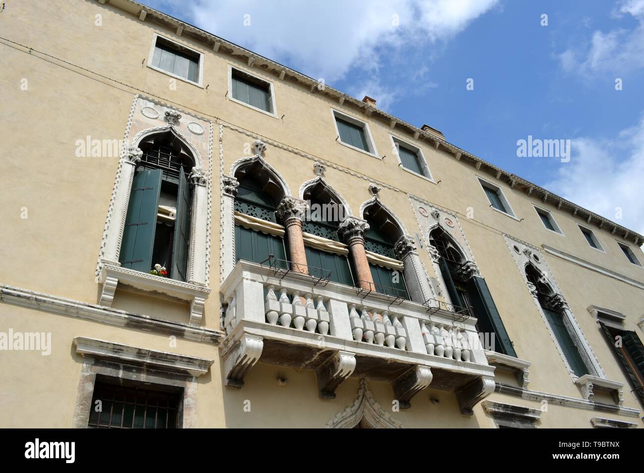 Bella vista in primo piano di un antico palazzo di Venezia in gotico veneziano lancet arch nello stile e decorate con un grande balcone e verde Vecchie persiane. Foto Stock