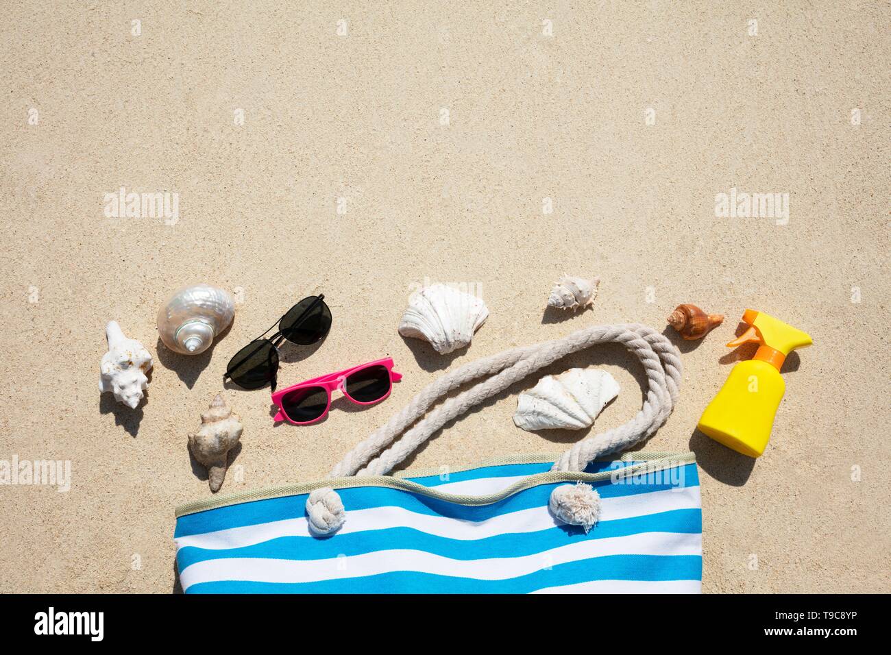 Conchiglie, occhiali da sole e crema solare, bottiglia e borsa sulla sabbia in spiaggia Foto Stock