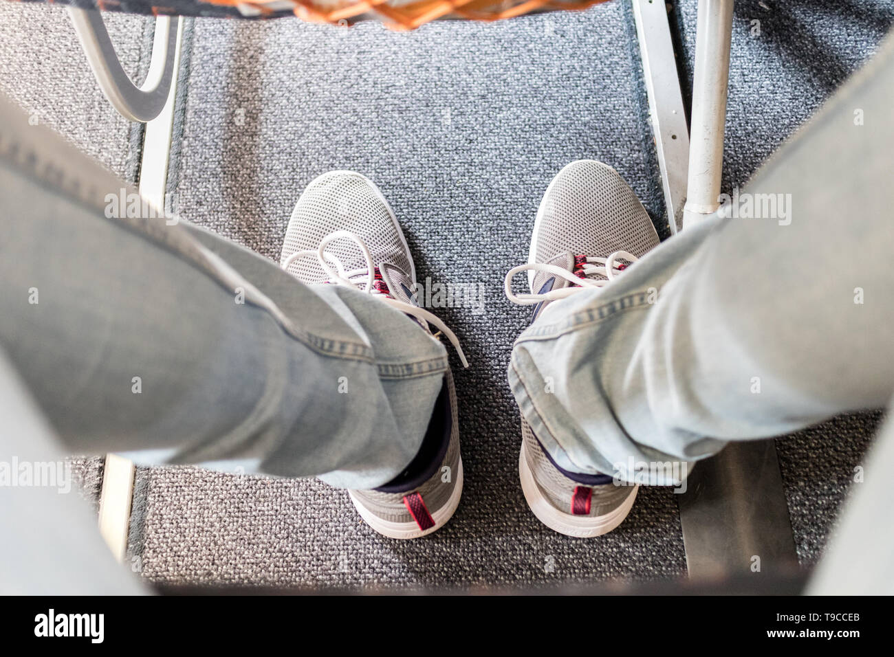 Passeggero maschio con la mancanza di spazio per le gambe sul commerciale lungo volo in aeroplano. Focus su casual sportivo sneakers Foto Stock
