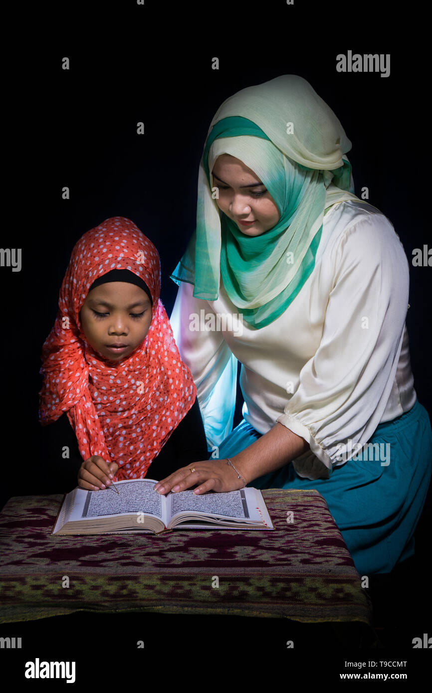 FLORES, INDONESIA-Giugno 25 2014: una sorella di hijab è di insegnare la sua sorella che indossa anche un hijab per leggere il Corano su una tabella con motivi etnici di saluti Foto Stock