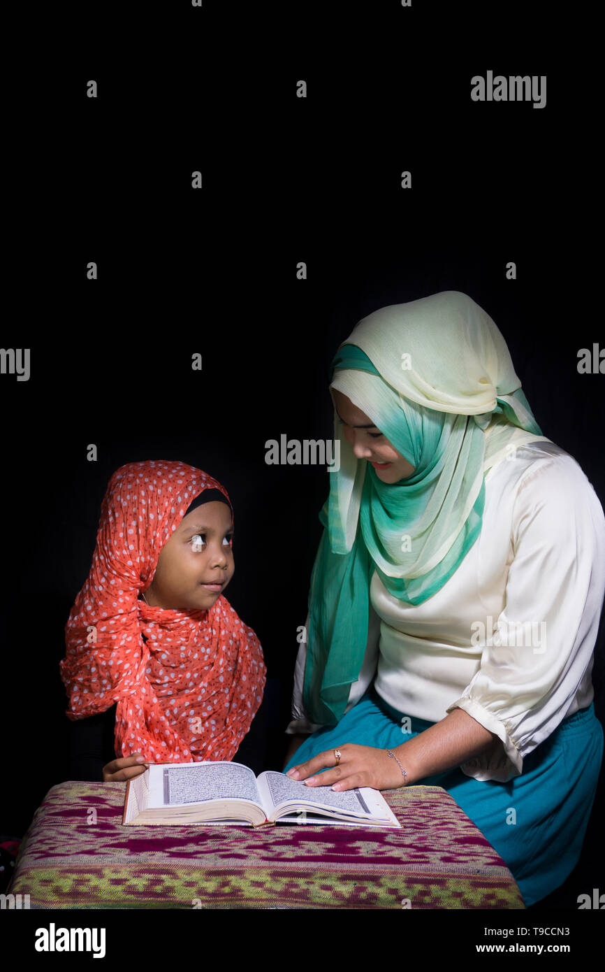 FLORES, INDONESIA-Giugno 25 2014: una sorella di hijab è di insegnare la sua sorella che indossa anche un hijab per leggere il Corano su una tabella con motivi etnici di saluti Foto Stock