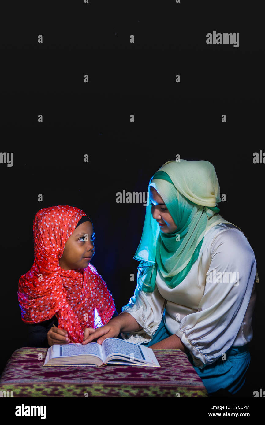 FLORES, INDONESIA-Giugno 25 2014: una sorella di hijab è di insegnare la sua sorella che indossa anche un hijab per leggere il Corano su una tabella con motivi etnici di saluti Foto Stock