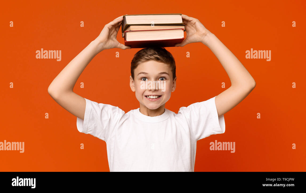 Scolaro positivo tenendo pila di libri sulla sua testa Foto Stock