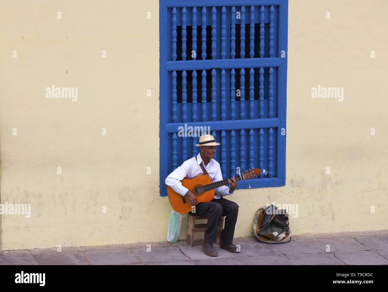 Anziani uomo cubano seduto e suonare la chitarra strumento su strade acciottolate della città vecchia di Trinidad, Cuba nei pressi di Plaza Mayor Foto Stock