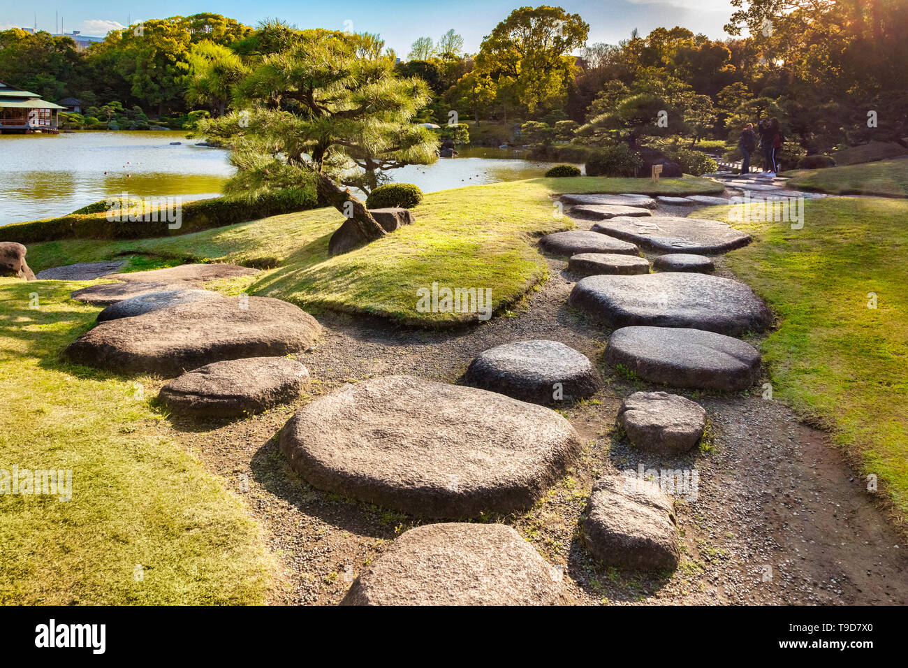 9 Aprile 2019: Tokyo, Giappone - Giardino Kiyosumi, pietre miliari accanto al lago. Flare come set di sole sulla parte in alto a destra. Foto Stock