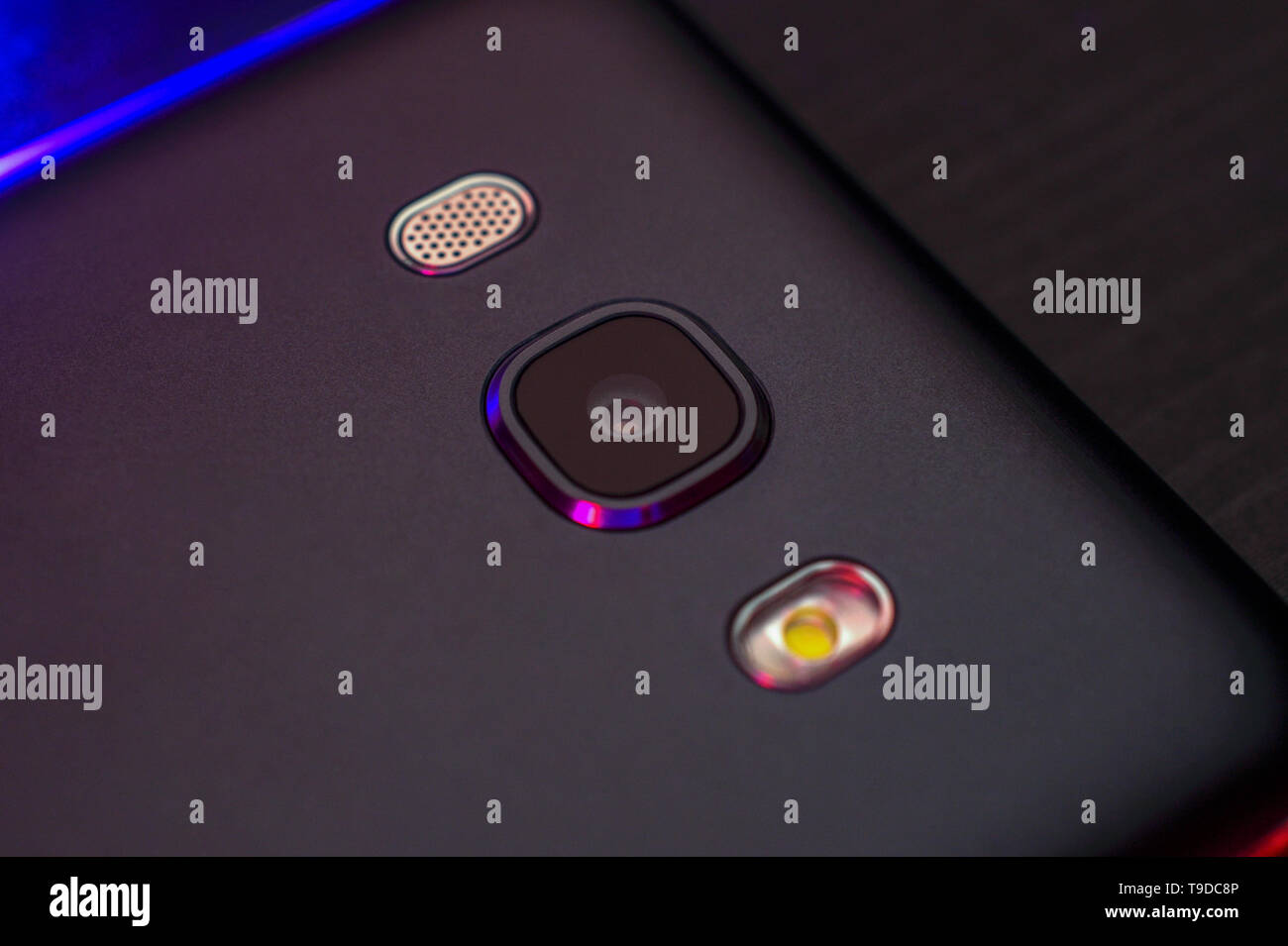 Close-up del telefono lente in nero scuro con retroilluminazione blu, vista dall'alto. Il lato inverso dello smartphone. Foto macro di un colore orizzontale. Foto Stock