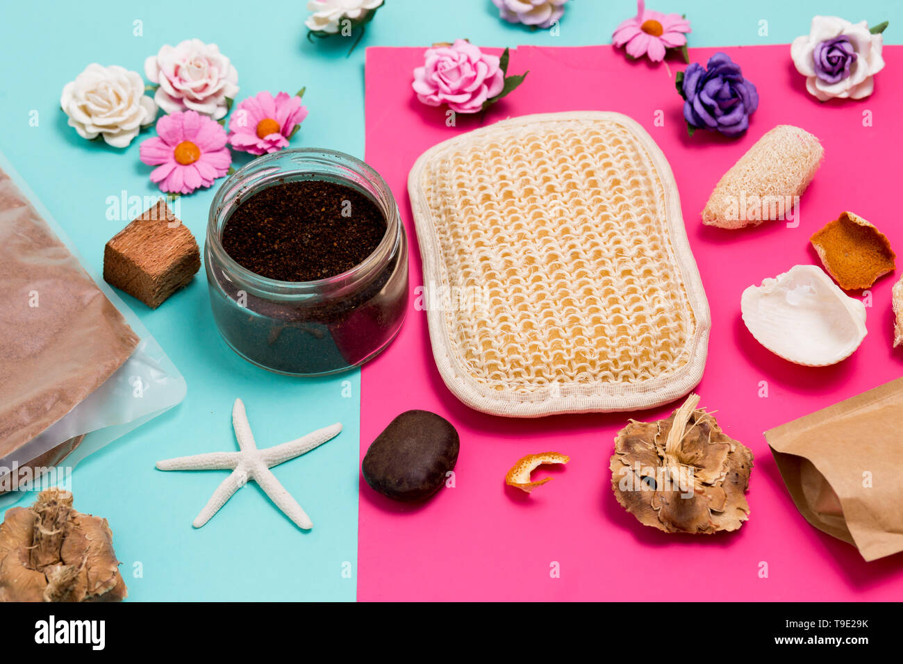 Primo piano della coloratissima Spa e di strutture di cura, piccoli fiori, scrub, toalhinha e conchiglie in rosa e sfondo blu Foto Stock