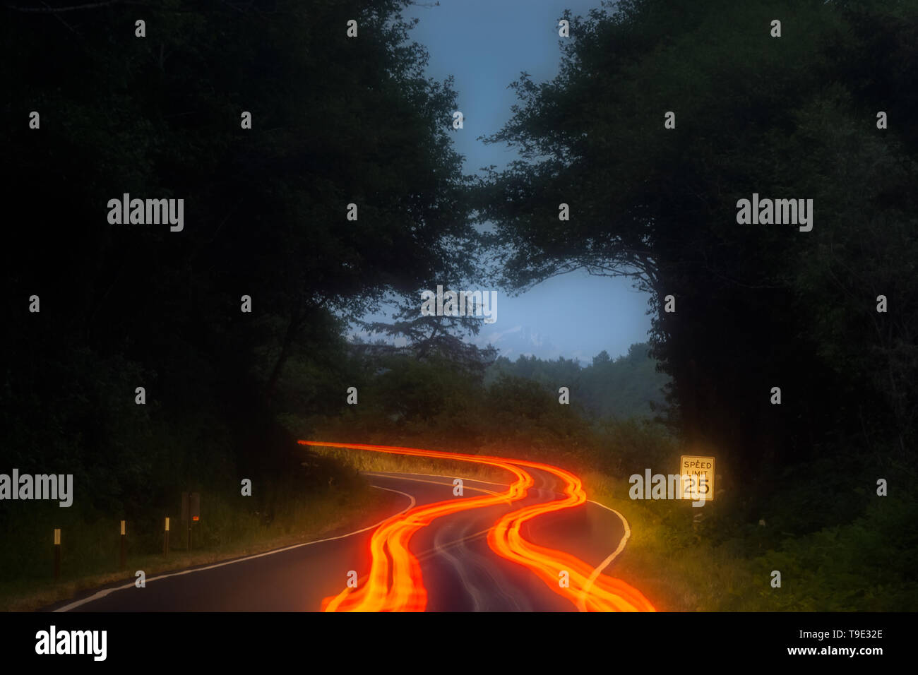 Arancione, rosso e giallo auto sentieri di luce lungo una strada curva in montagna di notte con il segnale di limite di velocità. Trasporto, guida e concetto di sicurezza Foto Stock