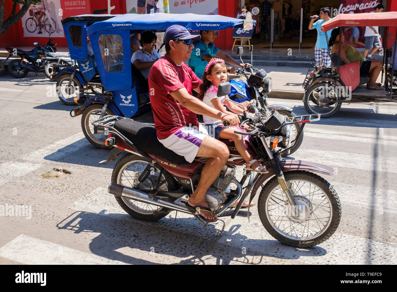 L uomo e la bambina (probabilmente padre e figlia) senza casco in sella a una motocicletta su strade trafficate di Yurimaguas, Regione di Loreto, Perù Foto Stock