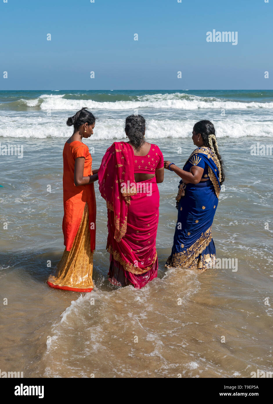 Tre donne stand in mare sulla baia del Bengala costa, Mahabalipuram (Mamallapuram), India Foto Stock