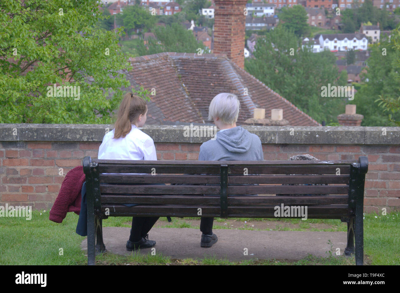 Vista posteriore di un caucasian ragazzo e ragazza sedeva su una panchina di Bridgnorth, Shropshire, Regno Unito Foto Stock