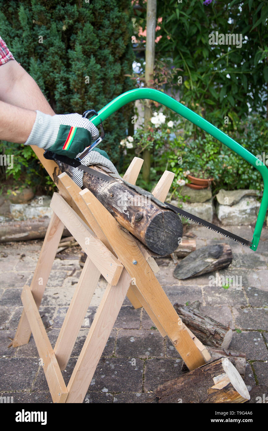 Segatura di legna da ardere manualmente con un seghetto a mano su una tavola di legno sawhorse Foto Stock