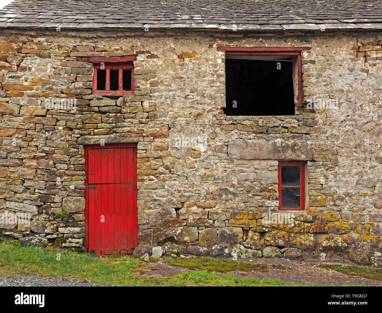 Antica pietra lichen coperti fienile con tetto in ardesia e stanco della vernice rossa sul legno irregolari in Cumbria,Inghilterra REGNO UNITO Foto Stock