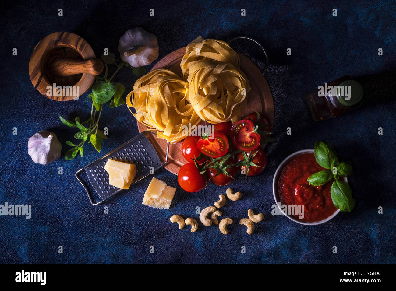 La tabella con gli ingredienti per fare il pesto di pomodoro. Pomodori, aglio, origano fresco e basilico erbe, bottiglia di olio d'oliva, alcune noci di acagiù, parmigiano, c Foto Stock