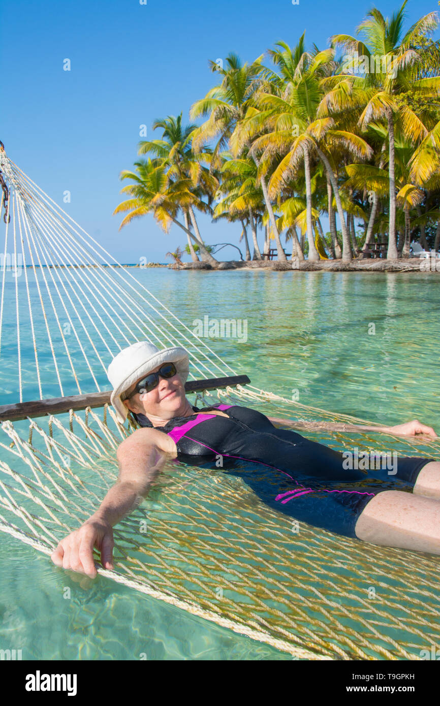 La donna gode di amaca in acque tropicali e piattaforme Palapa, a nord lungo il Coco Plum Caye Belize Foto Stock