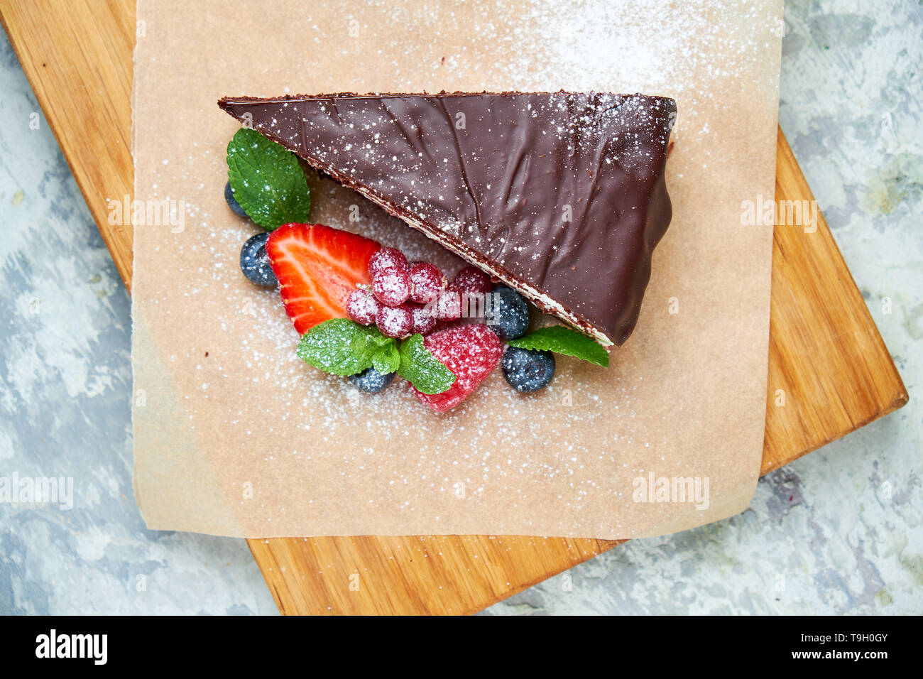 Una fetta di torta al cioccolato decorata con frutti di bosco su una tavola di legno. Grigio sfondo a trama. Bellissimi piatti di servizio. Il dessert. La catena alimentare Foto Stock
