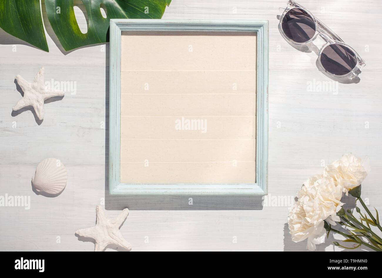 Vista superiore estate picture frame con foglie di monstera e conchiglia su bianco tavolo in legno duro con la luce d'ombra.vacanze estive Foto Stock