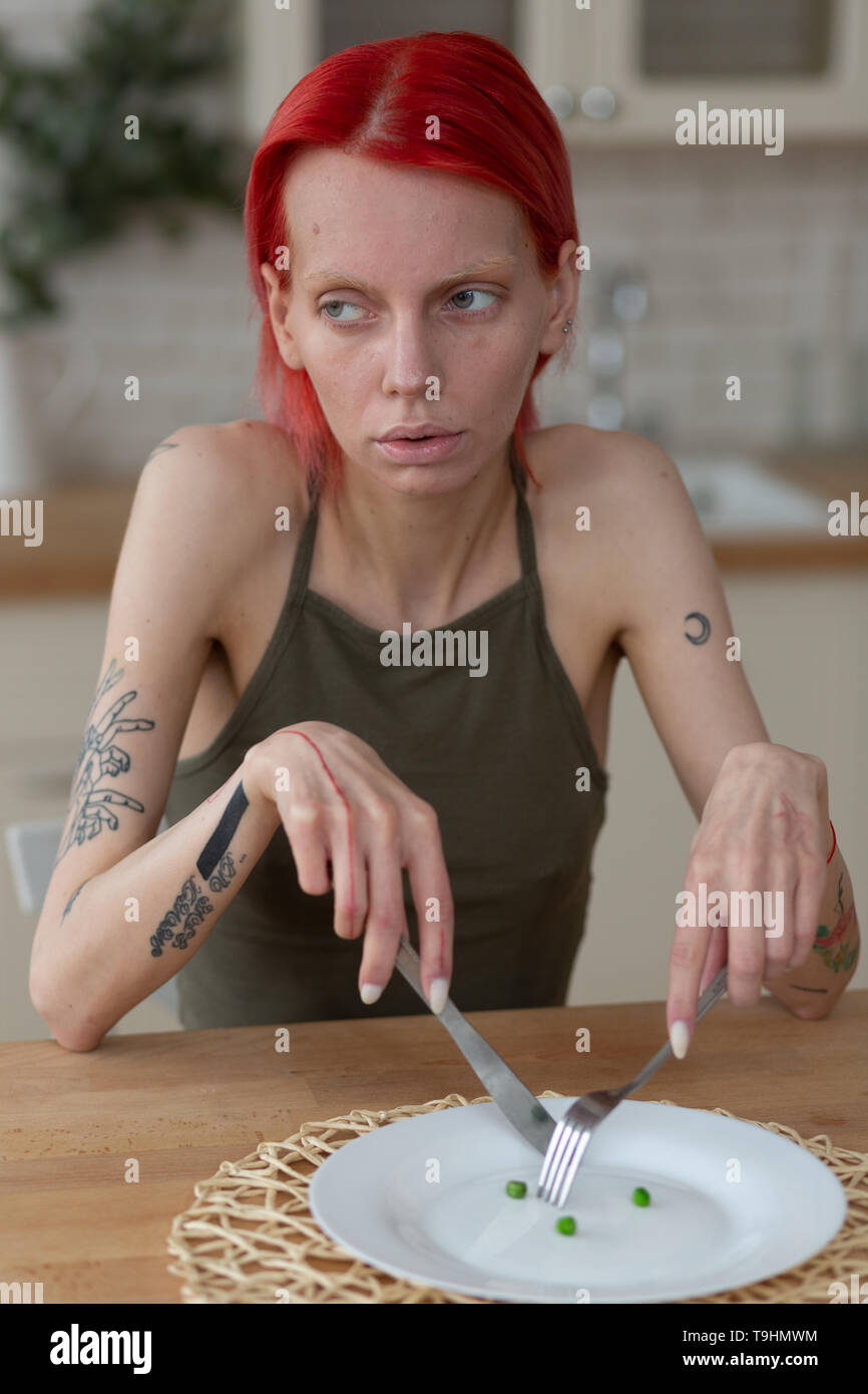 Skinny donna tenendo il coltello e forchetta seduta vicino la piastra a vuoto Foto Stock