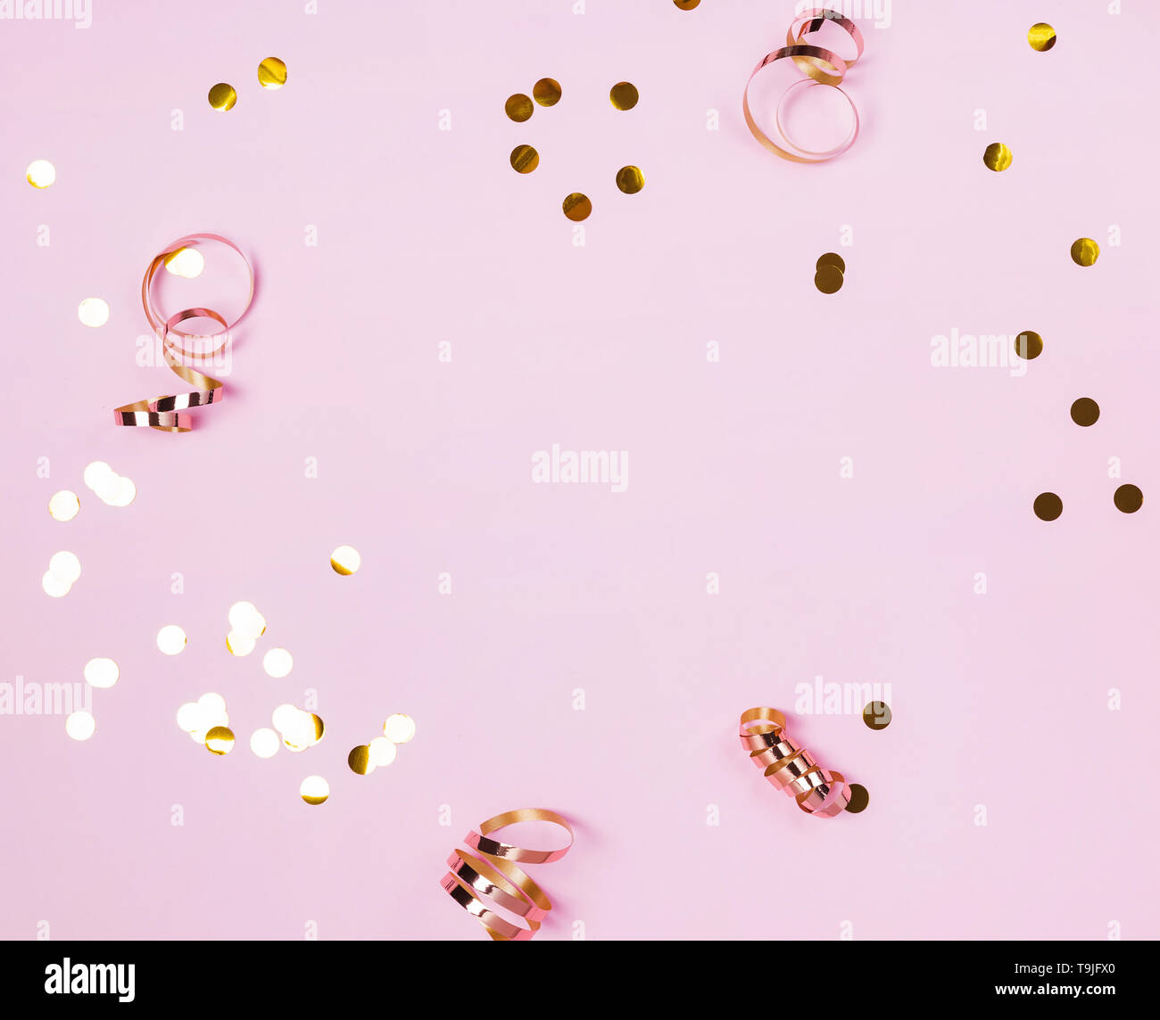 Shiny golden confeti e nastri su sfondo rosa. Cornice festosa. Foto Stock