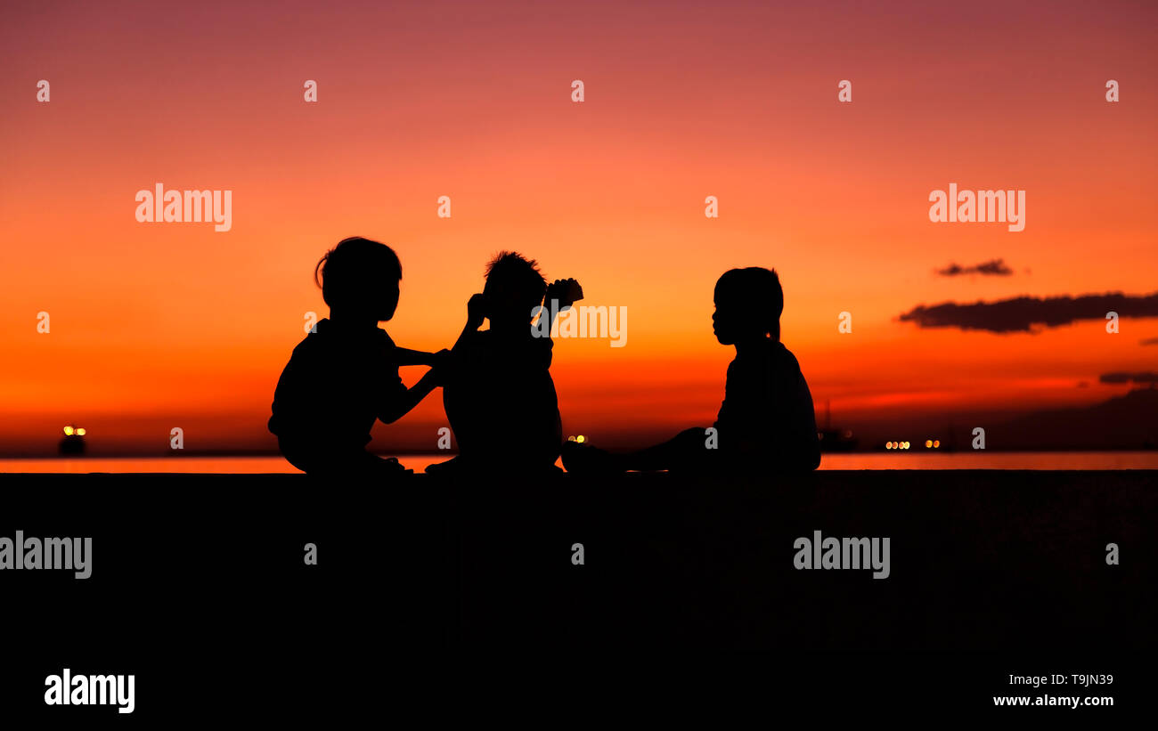 Sagome di bambini nel tramonto sul mare di Manila, Filippine Foto Stock