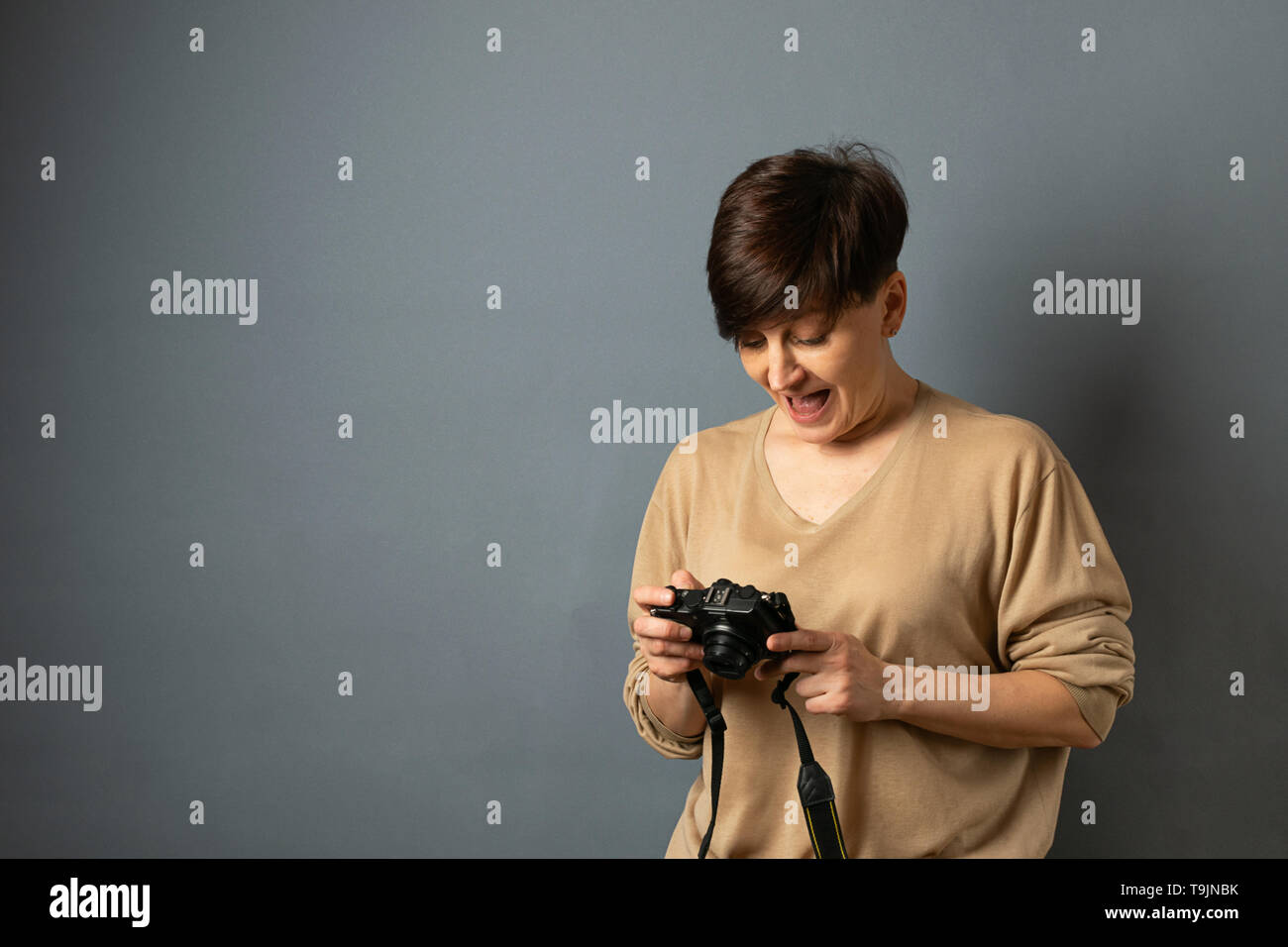 Una donna può contenere una fotocamera e guarda attraverso le foto. Ritratto di donna su sfondo grigio. Copia dello spazio. Foto Stock