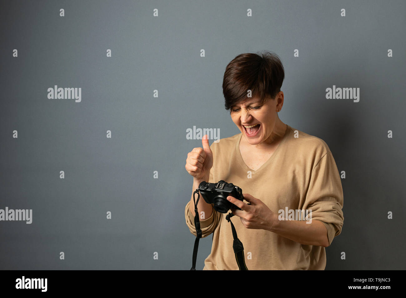 Una donna può contenere una fotocamera e guarda attraverso le foto. Ritratto di donna su sfondo grigio. Copia dello spazio. Foto Stock