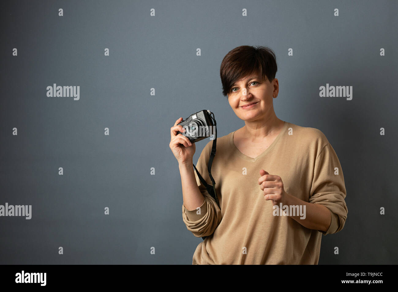 Una donna fotografo detiene una fotocamera . Ritratto di donna su sfondo grigio. Copia dello spazio. Foto Stock