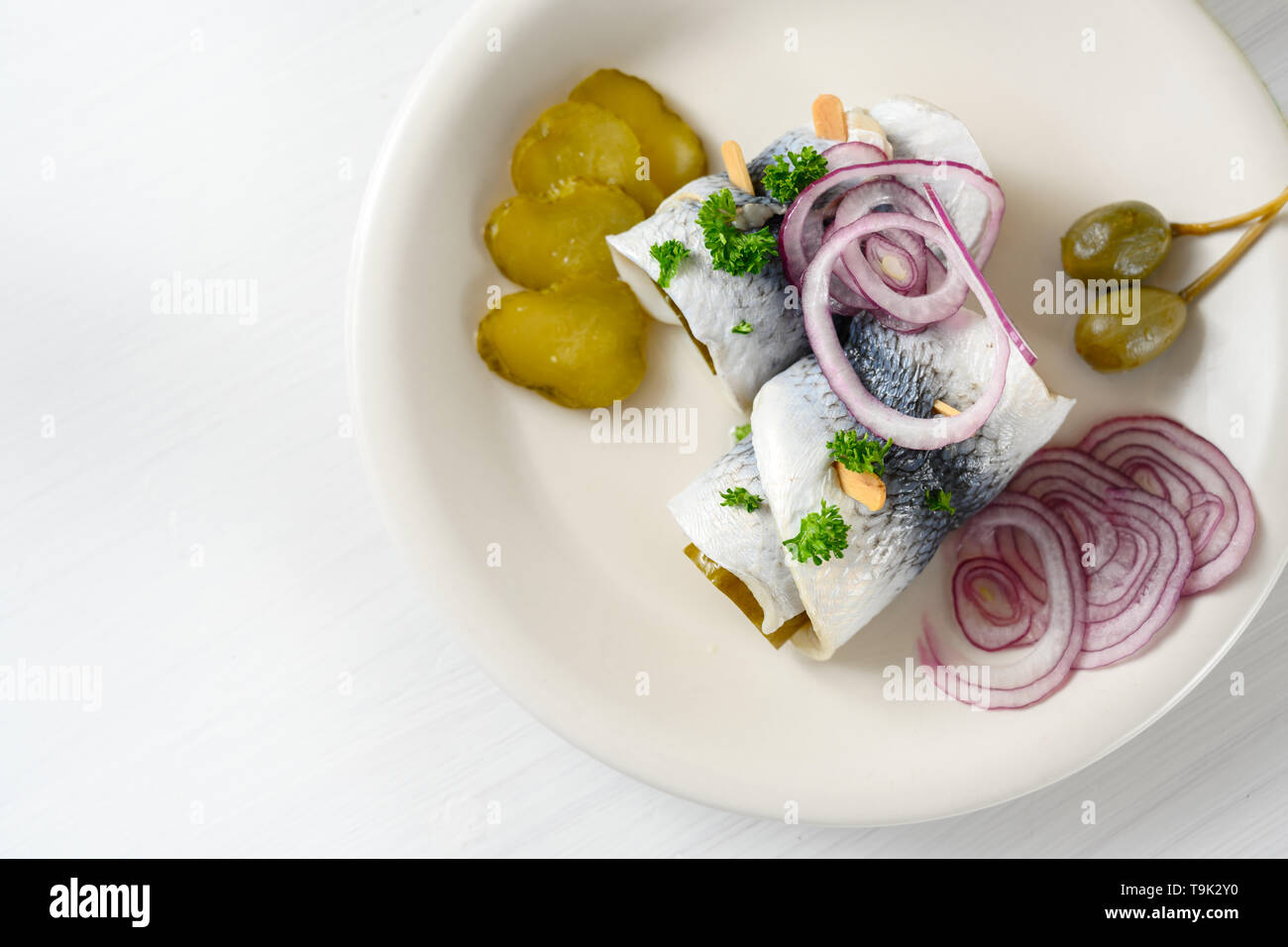 Decapato Laminato aringa, chiamato anche rollmops con cipolle rosse, cetriolini e capperi, un aspro sbornia colazione su un tavolo bianco, ad alto angolo di visione da ab Foto Stock