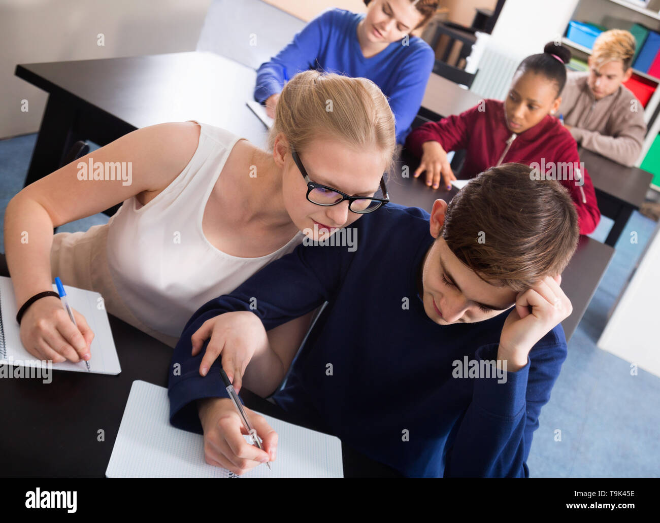 Efficiente studentessa guardando il test variante del suo vicino di casa nella classe Foto Stock