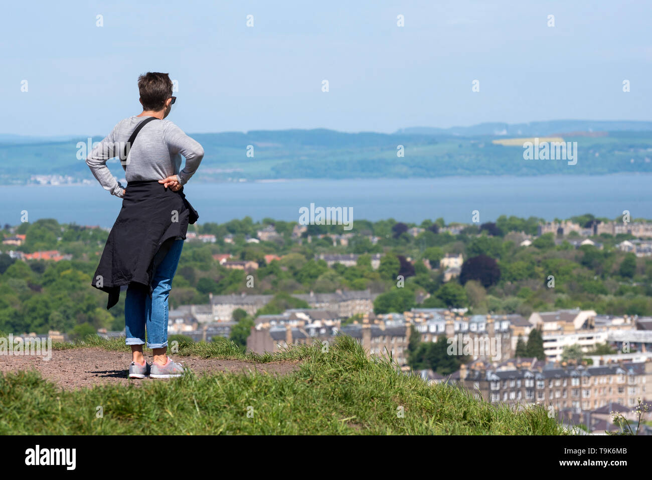 Una donna si erge su Calton Hill prendendo le vedute del Nord di Edimburgo, Leith e sul Firth of Forth. Foto Stock