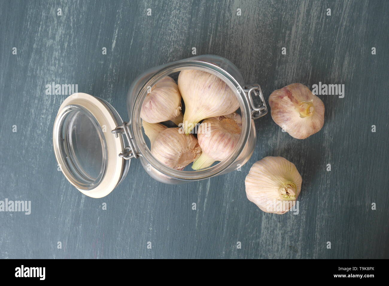 Capi di aglio in un vaso kilner su un blu in legno invecchiato tavolo da cucina. Foto Stock