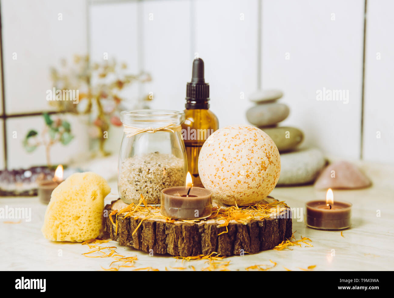 Vista laterale di home wellness spa prodotti bagno arancione bomba, bagno aromatico sale, spugna del mare, tè candele accese. Molto zen impostare, albero di amore e ametista cryst Foto Stock